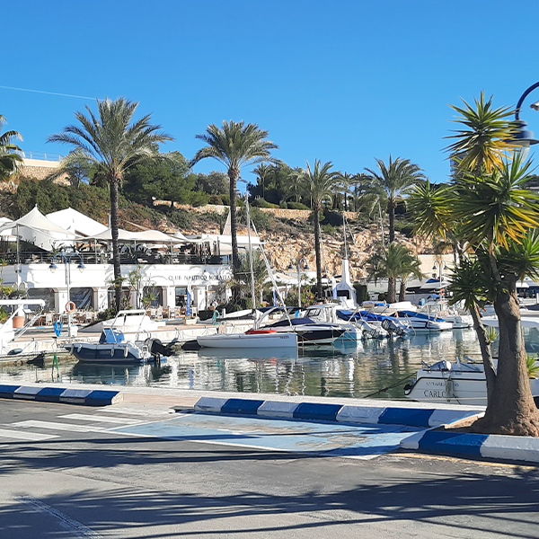 Zonnig zicht op de exclusieve Club Náutico in Moraira met luxe jachten en palmbomen, dé hotspot voor gastronomie vlak bij investeringsproject Cala Natura Benissa.