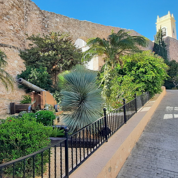 De historische stadsmuren en tuinen in het oude centrum van Calpe met uitzicht op de kerktoren, een populaire culturele bezienswaardigheid vlak bij investeringsproject Cala Natura.