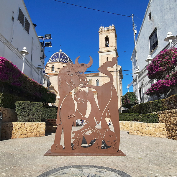 Kunstwerk op het kerkplein van Altea met de iconische blauwe koepelkerk op de achtergrond, een populaire culturele trekpleister vlak bij Cala Natura.